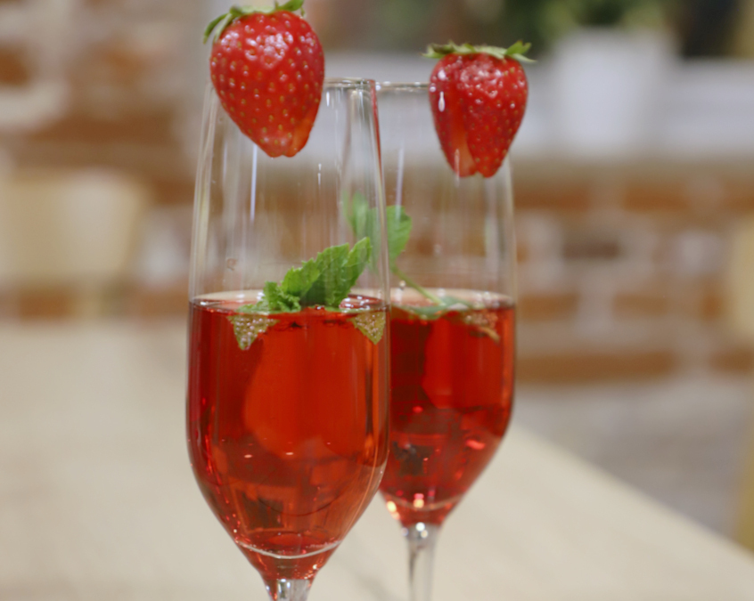 Two sparkling wine glasses filled with sparkling wine and garnished with strawberries.