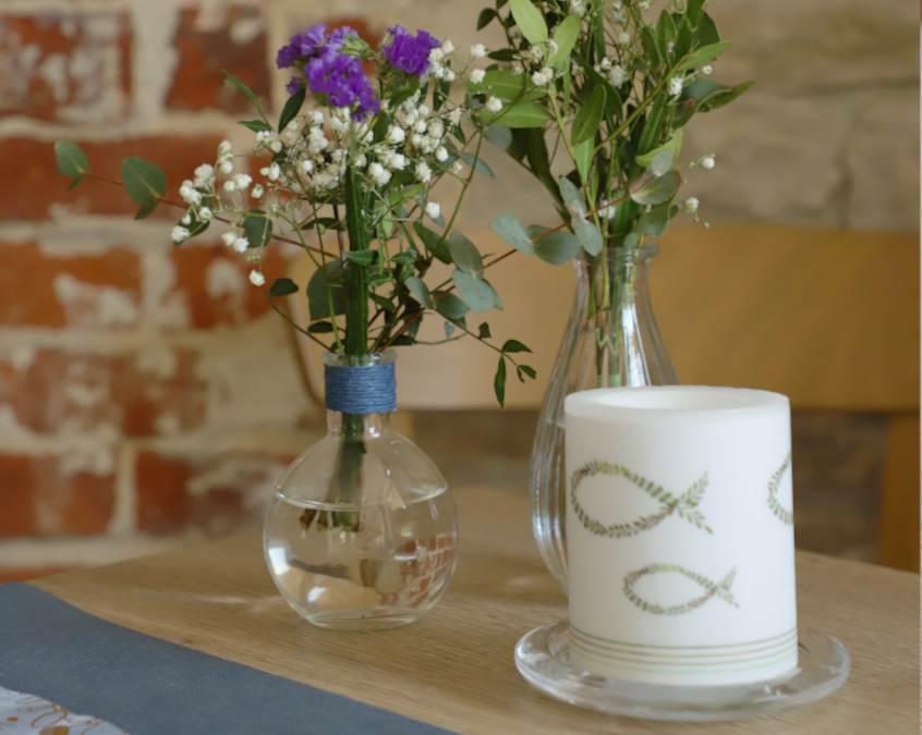 Candle and two flower vases with flowers, themed for a baptism.